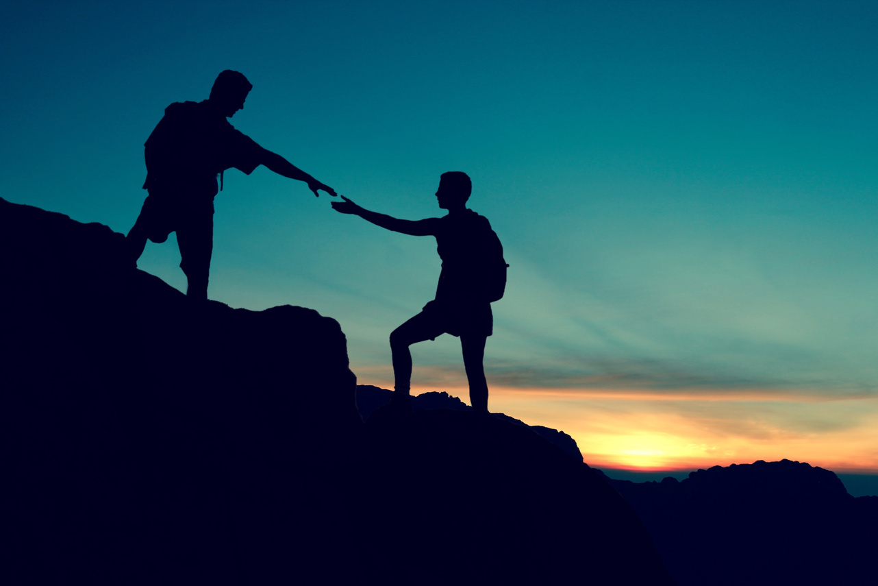 silhouette of two people on top of a mountain at sunset