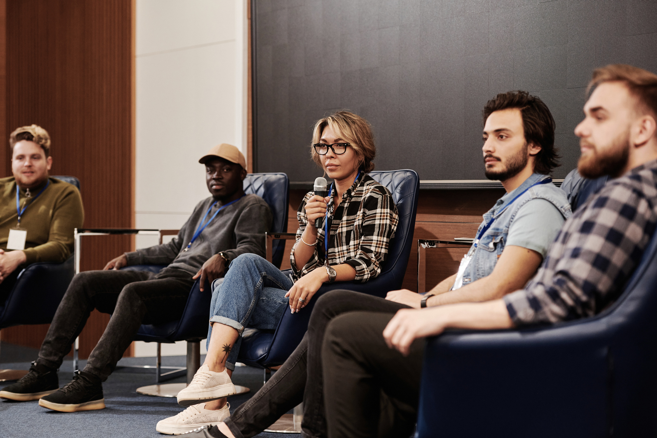 a group of speakers sitting on chairs in front of a screen